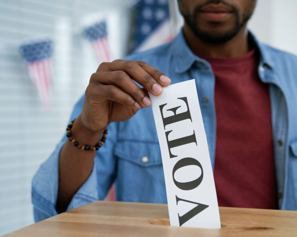 Image of a Black man putting a piece of paper with the word VOTE on it into a box. Black Millenial and Gen Z voters were significant in the 2024 election. 