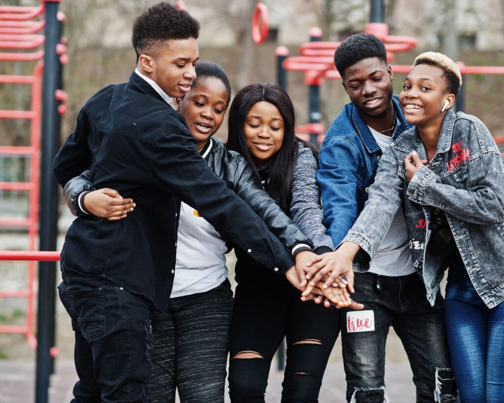 Image of five young Black men and women putting one of their hands on top each of the others in a team stance. They are all smiling and standing outside in what appears to be a playground. A political analyst says data shows that young Black Millenial and Gen Z voters sat out the 2024 election causing the Democrats to lose.