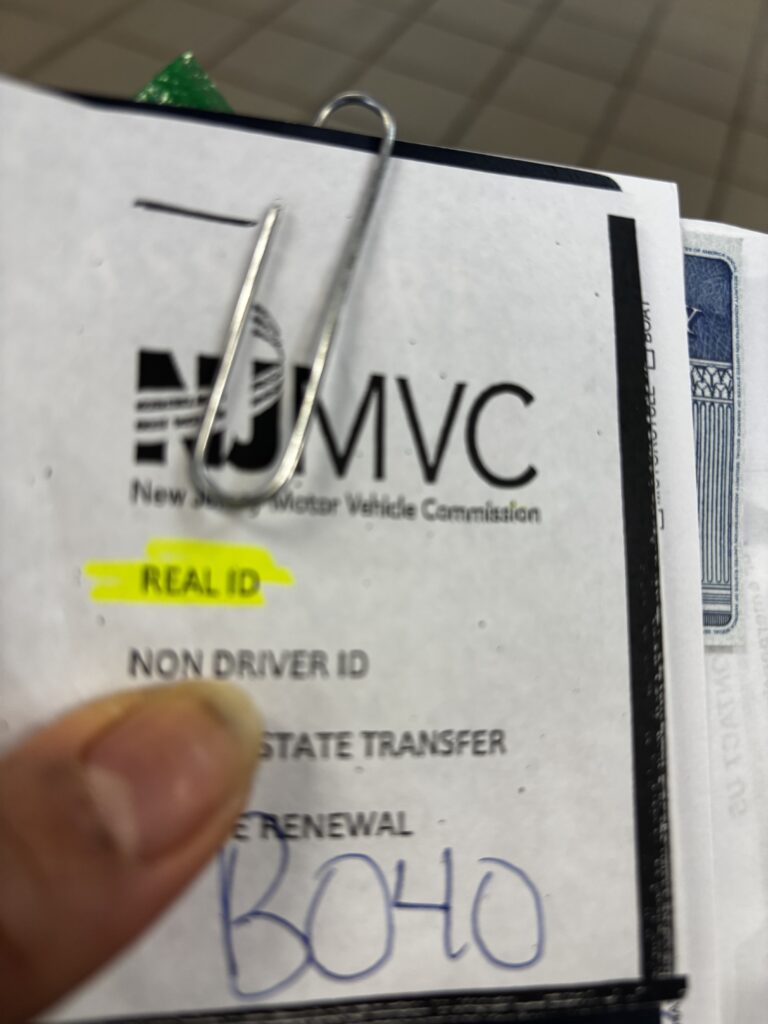 Several paper documents held together with a paper clip. The iem on top says NJMVC which stands for New Jersey Motor Vehicle Commission. Highlighted in yellow on that paper are the words REAL ID.